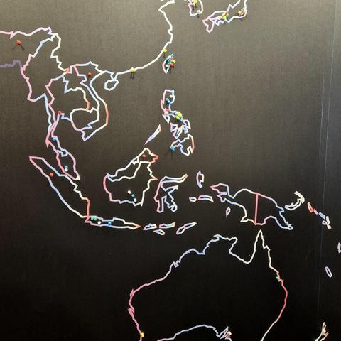 Large wall map Australasia with a black background and country borders highlighted in white-dominant neon colors. Many places have push pins.
