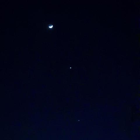 Slightly out-of-focis and grainy shot of a waxing crescent Moon, Venus, and Jupiter against a deep blue twilight sky