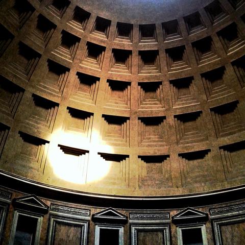 Saturated and high contrast photo of a portion of the domed ceiling of Rome’s Pantheon with the circular sunlight from the off-frame oculus hitting the ceiling and providing a dramatic interplay of light and shadow on the ceiling’s coffers