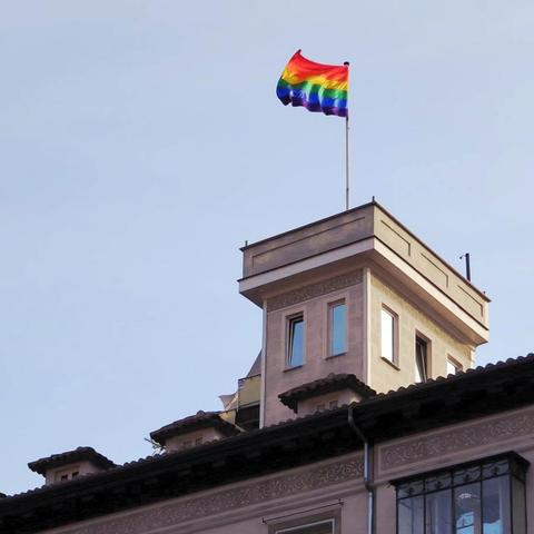 Rooftop edge with a small rectangular one-story flat-topped tower over it and with a rainbow-striped flag flying on a pole on top of the tower