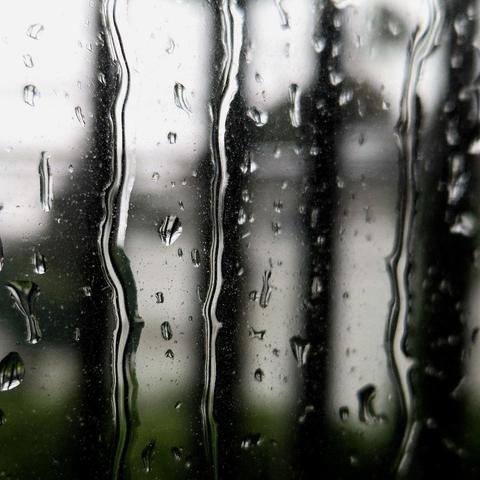 Macro photograph focused on rain streaks streaming down a glass pane with the outside scenery very blurry and indistinct