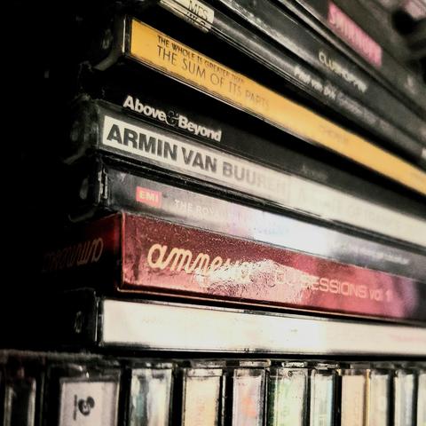Close-up photo of several CD cases stacked horizontally with their spine labels facing the light. They are sitting on top of more CD cases stacked vertically. Some visible artist names are Armin van Buuren, Paul van Dyk, and Above & Beyond.