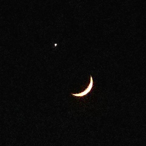 Grainy night sky photo of a crescent moon with the bright side facing the bottom right and a bright Venus approximately half a degree to the upper-left of the moon