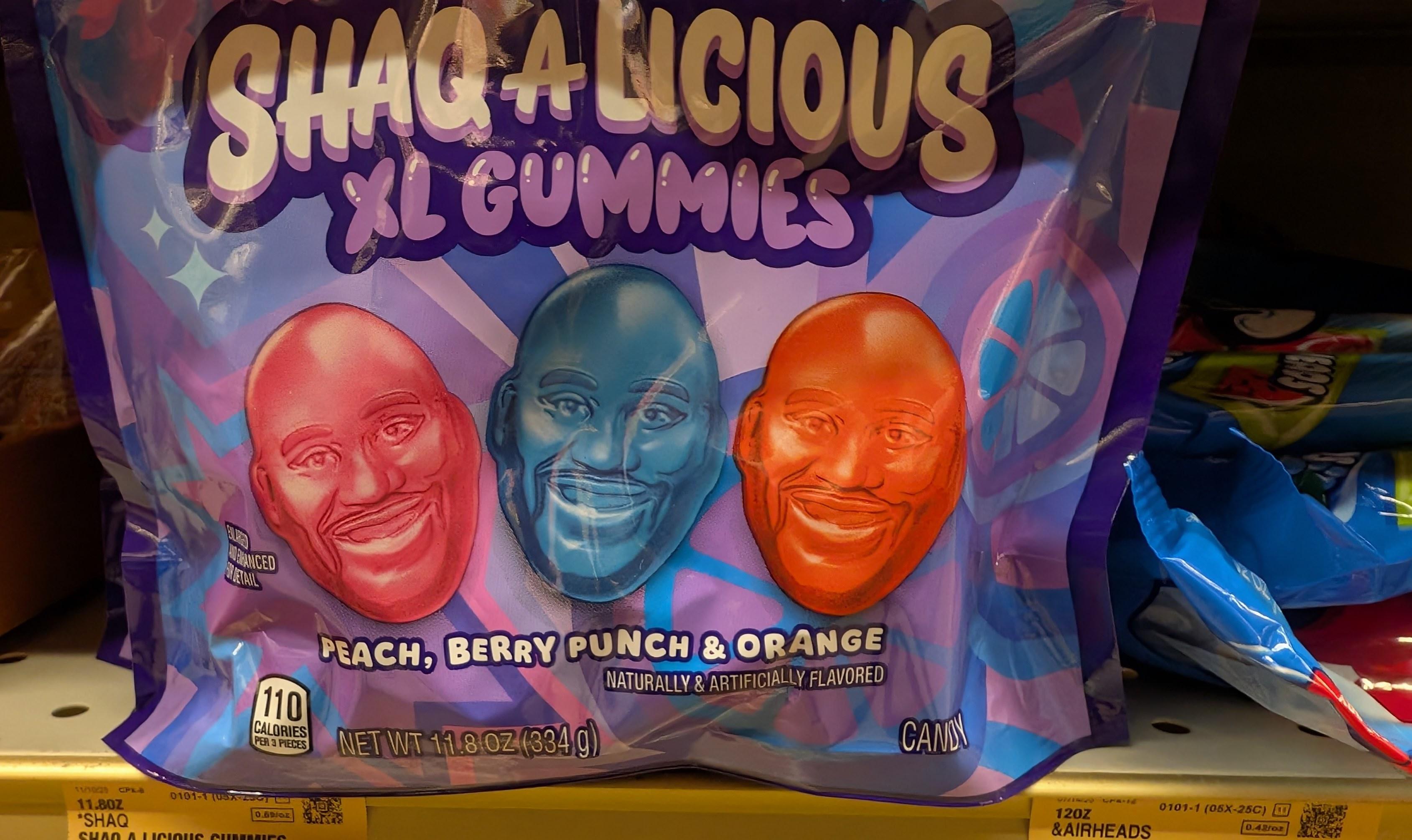 A package of "Shaq-a-licious XL Gummies". Its a colorful but slightly garish bag with three smiling Shaquille O'Neal heads as gummies in the flavors of peach, berry punch, and orange.