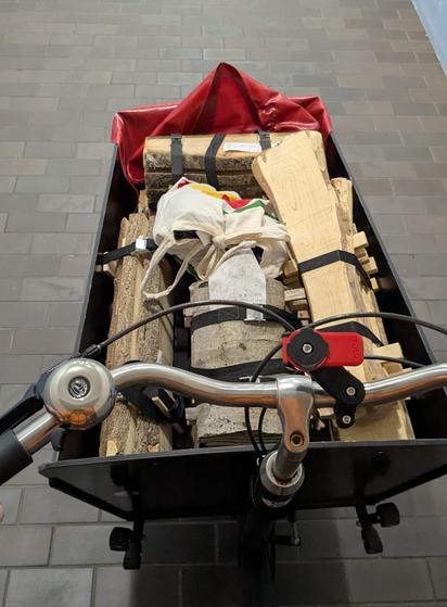The cargo box in front of the handlebars of a Long-John-style cargo bike sits full with neatly bundled stacks of small sawn and dried wooden boards.