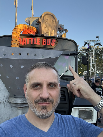 A selfie of me in front of the Fortnite battle bus, pointing up as the battle bus sign on the front.