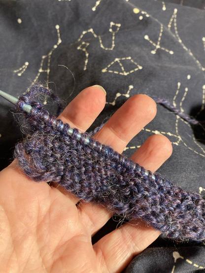 My hand showing maybe eight lines of knitting with purple fuzzy thread on one knitting needle. It's not great but it's okay!