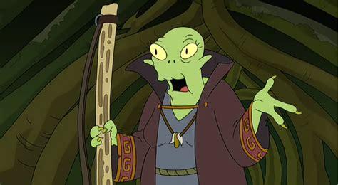 The Grand Midwife / Grand Priestess / Grand Lunch Lady / Grand Funeral Director / Grand Parking Validator / Grand Butterfly Curator, from Futurama. She's an amphibiosan, wearing ceremonial robes and carrying a wooden staff.