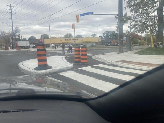 We are at a light. A concrete corner has been placed on the other side of a crosswalk, with space between it and the street corner, accommodating the bike lane to our right.