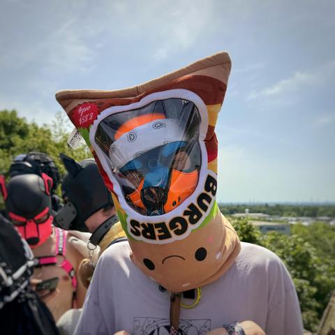 Aki wearing HeRO's plushie burger bar as a helmet looking put through the plastic window
