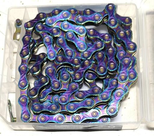 A brand new, pre-waxed, KMC 11 speed bicycle chain sits in its open plastic packing. A set of joining links is included, and visible at top and bottom left.

Unusually, the chain plates are mostly purple edged with blue edging, with dashes of yellow-gold. It looks almost tie-dyed.