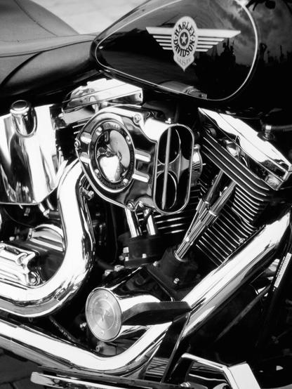 The "analog" black and white photograph shows a detail of the engine assembly of a "Harley-Davidson" motorcycle with its gleaming chrome.