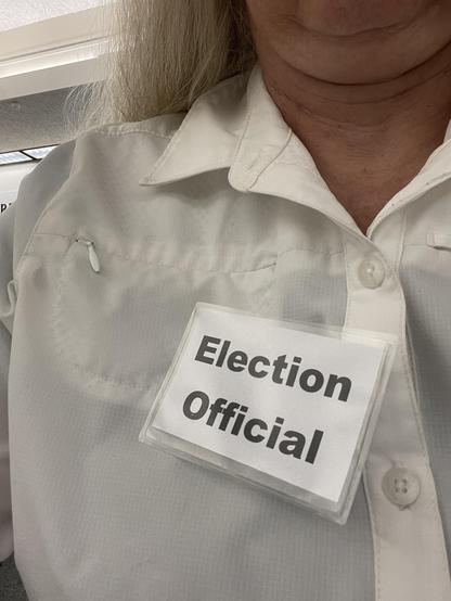 A person wearing a white shirt with a name tag that says Election Official.