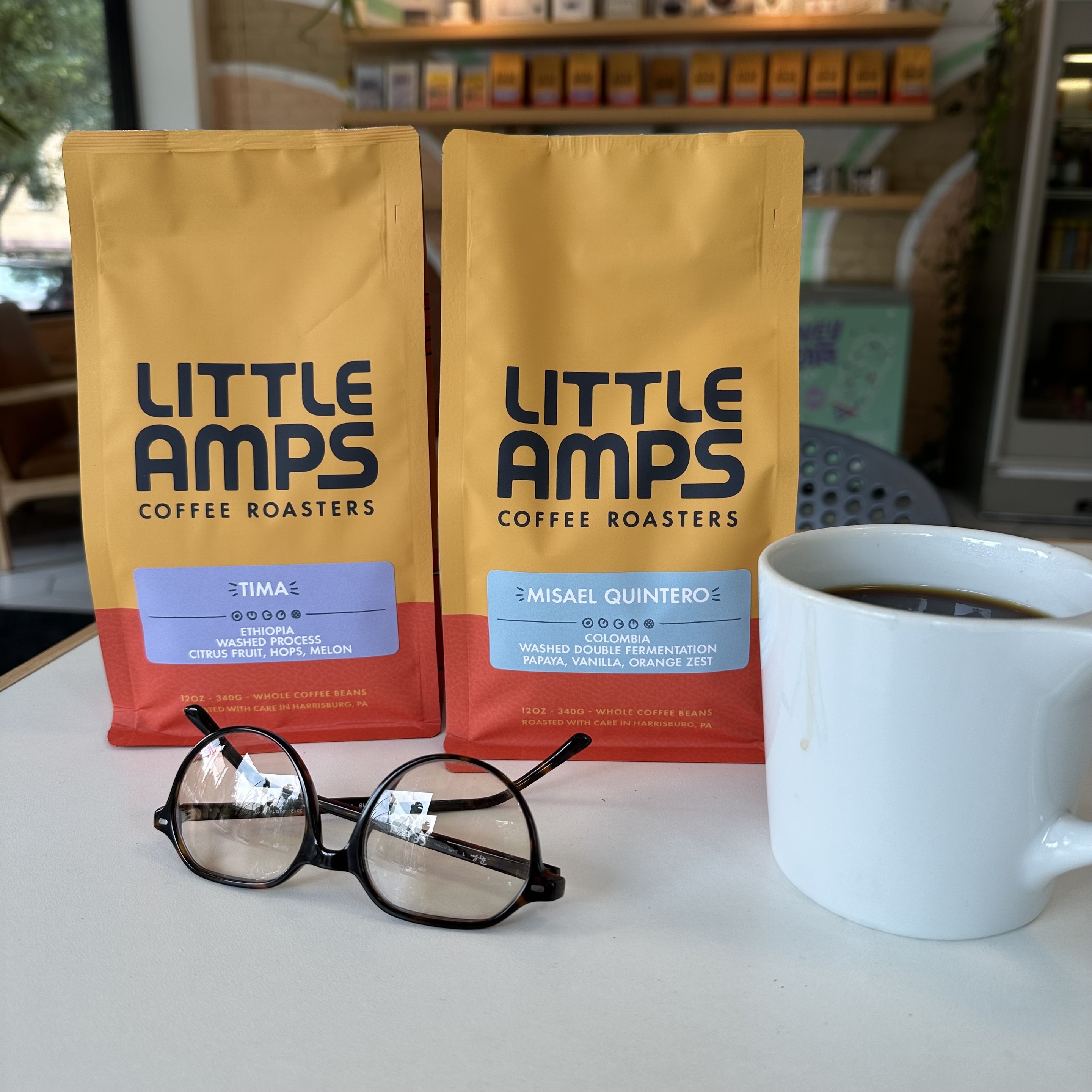 Color photo of two bags of Little Amps roasted coffee beans, sitting on a round white table, next to a white cup of coffee and a pair of eye glasses reflecting light from the shop’s windows. Harrisburg PA

The coffee bags are bright yellow on top (about three quarters of the bag height) with Little Amps printed in rounded modern black letters. The bottom of the bag is red. The coffee description is written in white letters on a grey sticker centered on the yellow / red boundary.

Great beans

TIMA — ETHIOPIA
WASHED PROCESS
CITRUS FRUIT, HOPS, MELON

MISAEL QUINTERO — COLOMBIA
WASHED DOUBLE FERMENTATION PAPAYA, VANILLA, ORANGE ZEST