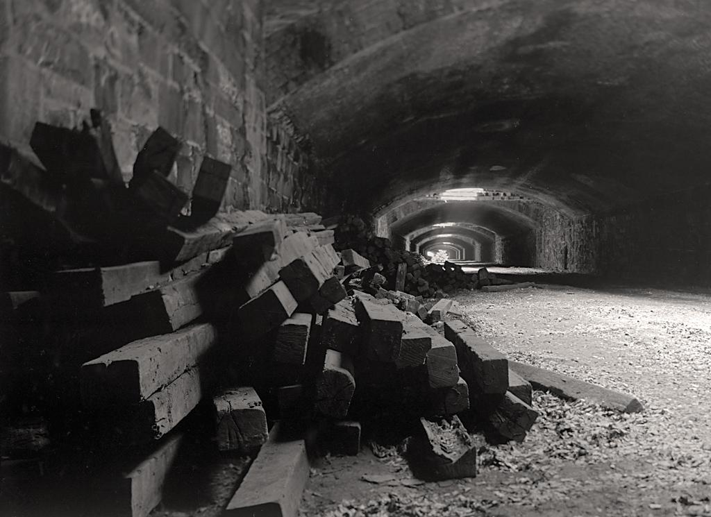 Interior of abandoned railroad tunnel with arched ceilings and grates admitting light at intervals. A stack of railroad ties is in foreground left. Interior of abandoned railroad tunnel with arched ceilings and grates admitting light at intervals. A stack of railroad ties is in foreground left.
