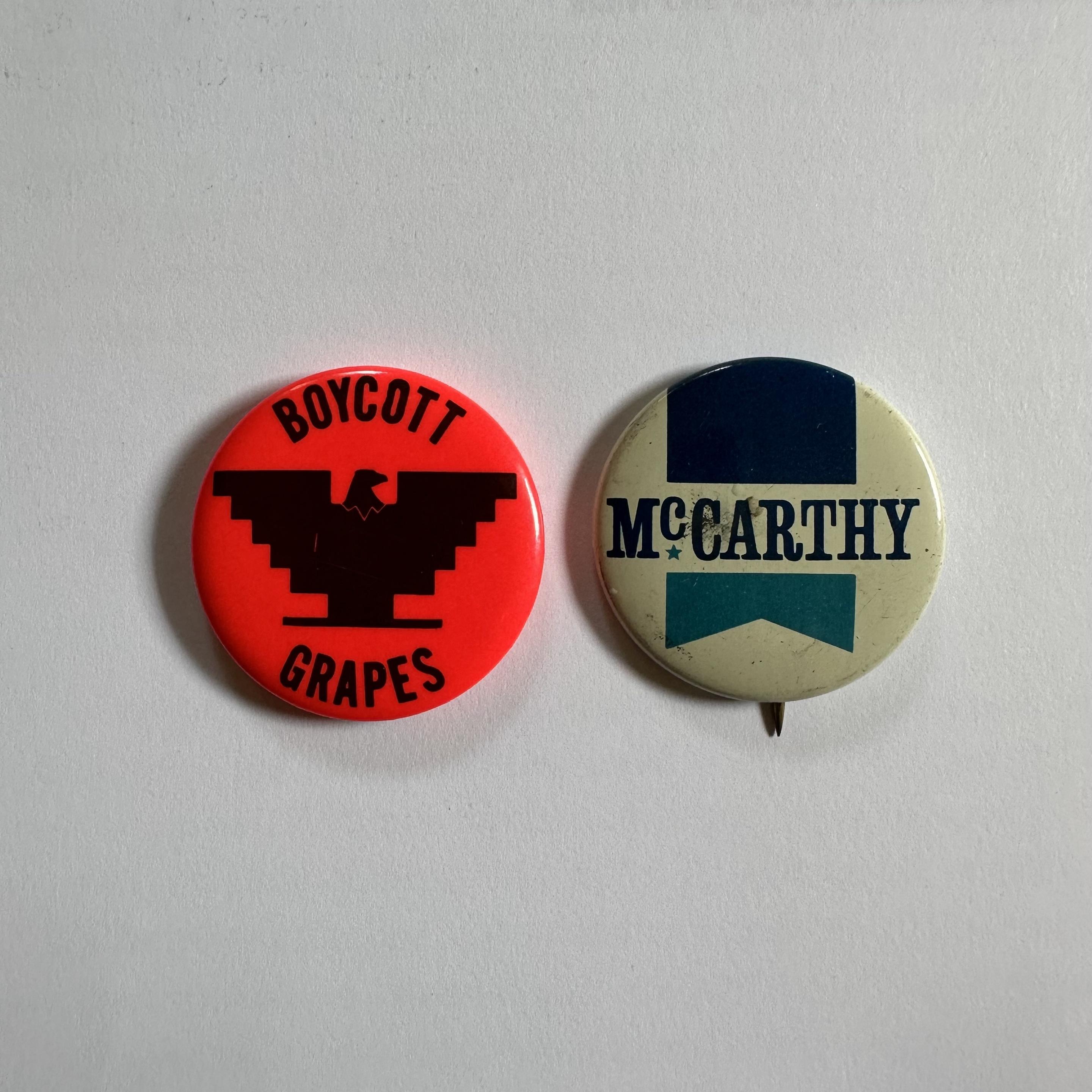 Color photo of two circular pin-on buttons: 1969 bright orange button with black Boycott Grapes curving around the top and bottom halves of the button, surrounding the American Farm Workers eagle logo; 1968 white McCarthy campaign button with McCarthy in black letters over a dark blue and turquoise vertical ribbon, with a triangular notch at the ribbon鈥檚 bottom.