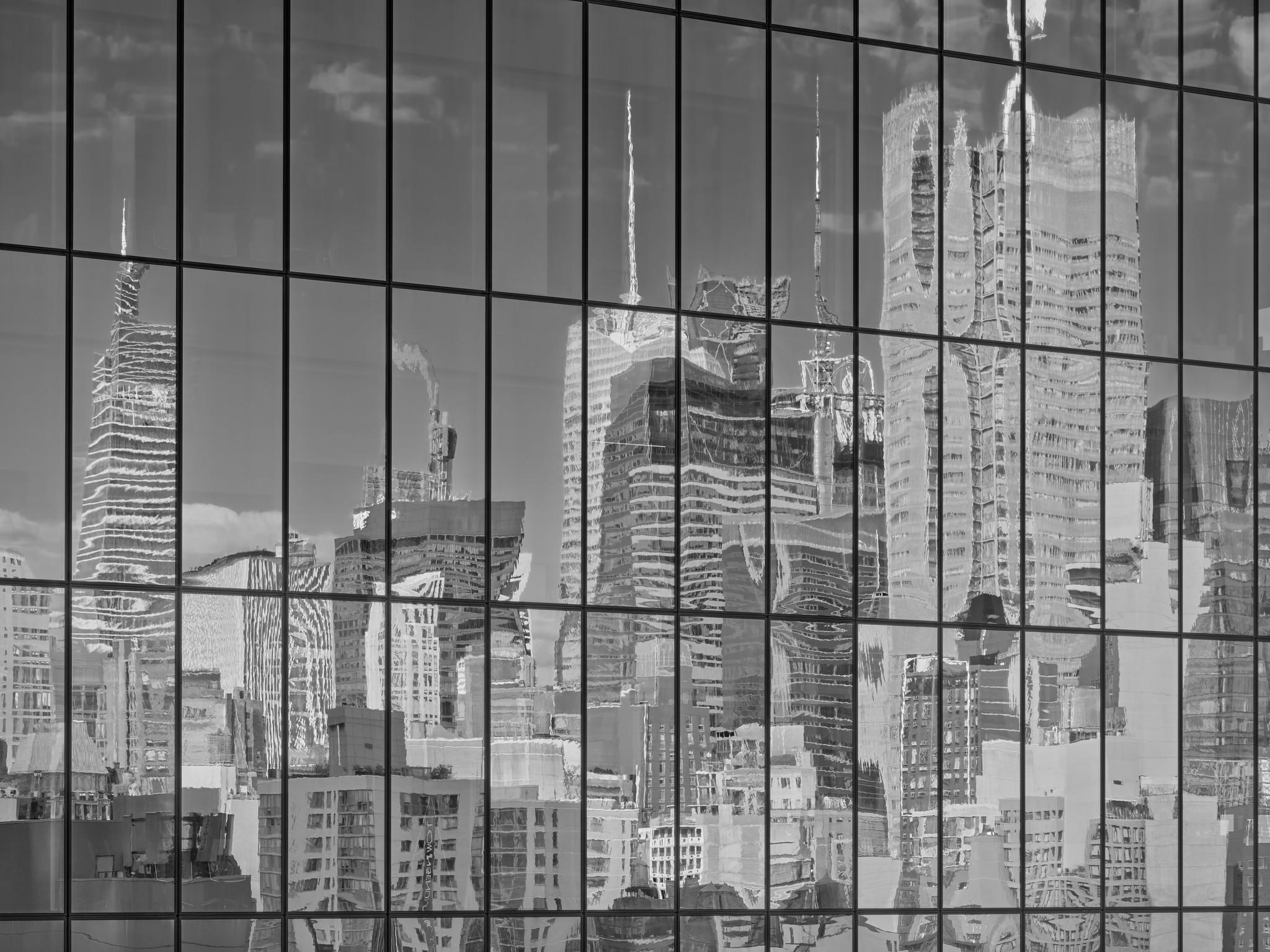 Abstract photo of the side of a glass curtain office building, with a grid formed by window sections, showing a distorted reflection of a crowded skyline of skyscrapers