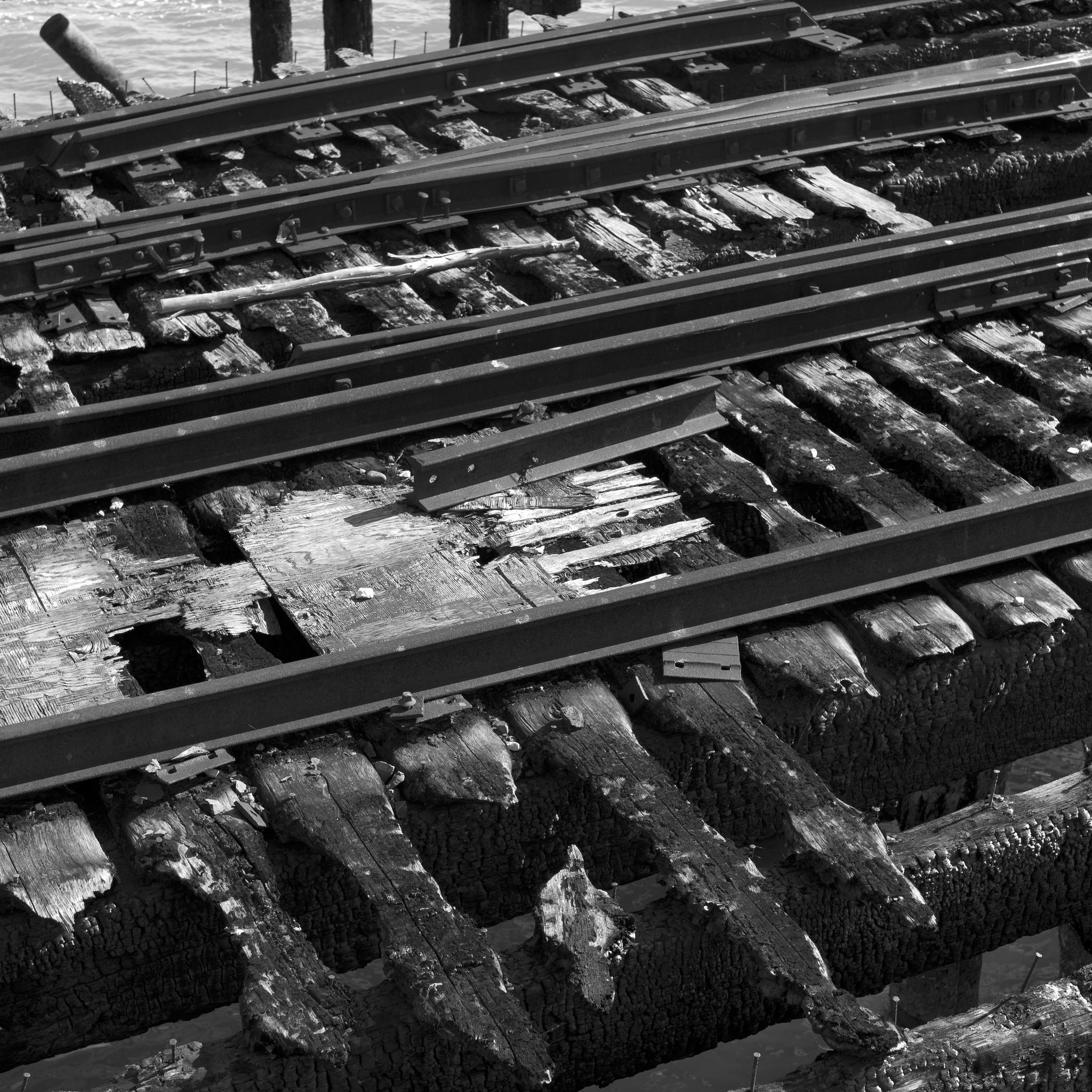 Detail of railroad tracks and charred wooden ties on a pier.