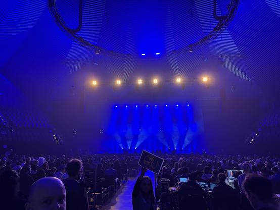 Empty stage with blue lighting, expectant audience seared in front.