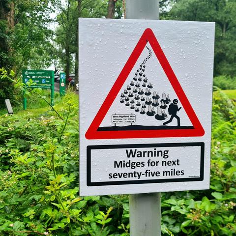 A road sign showibg a person with a backpack being pursued by a horde of midges. Below are the words Warning: Midges for next seventy-five miles.