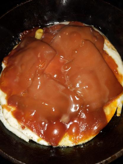 An egg fries while Brown Cheese melts and bubbles on top