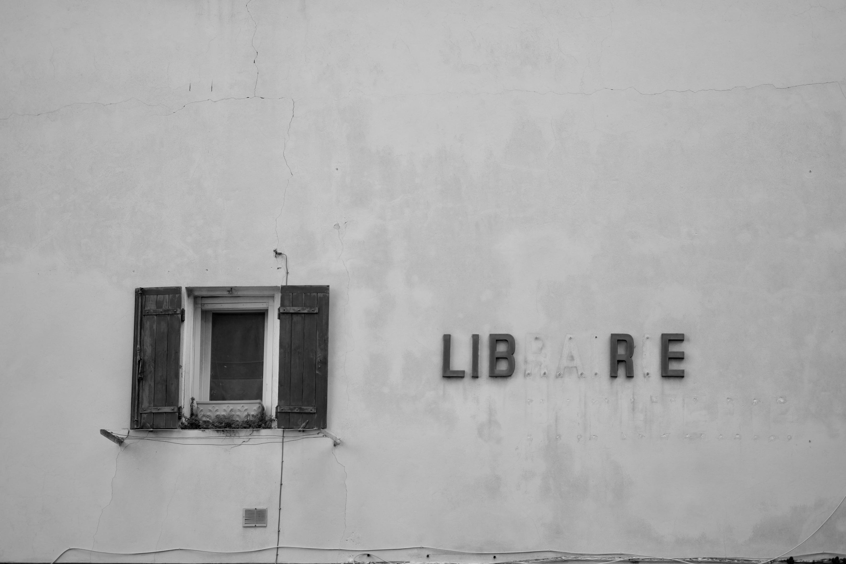 Photo en noir et blanc d'un mur avec une fenêtre et à côté, là où il y avait inscrit LIBRAIRIE, il n'y a plus que les lettres qui forment LIBRE.