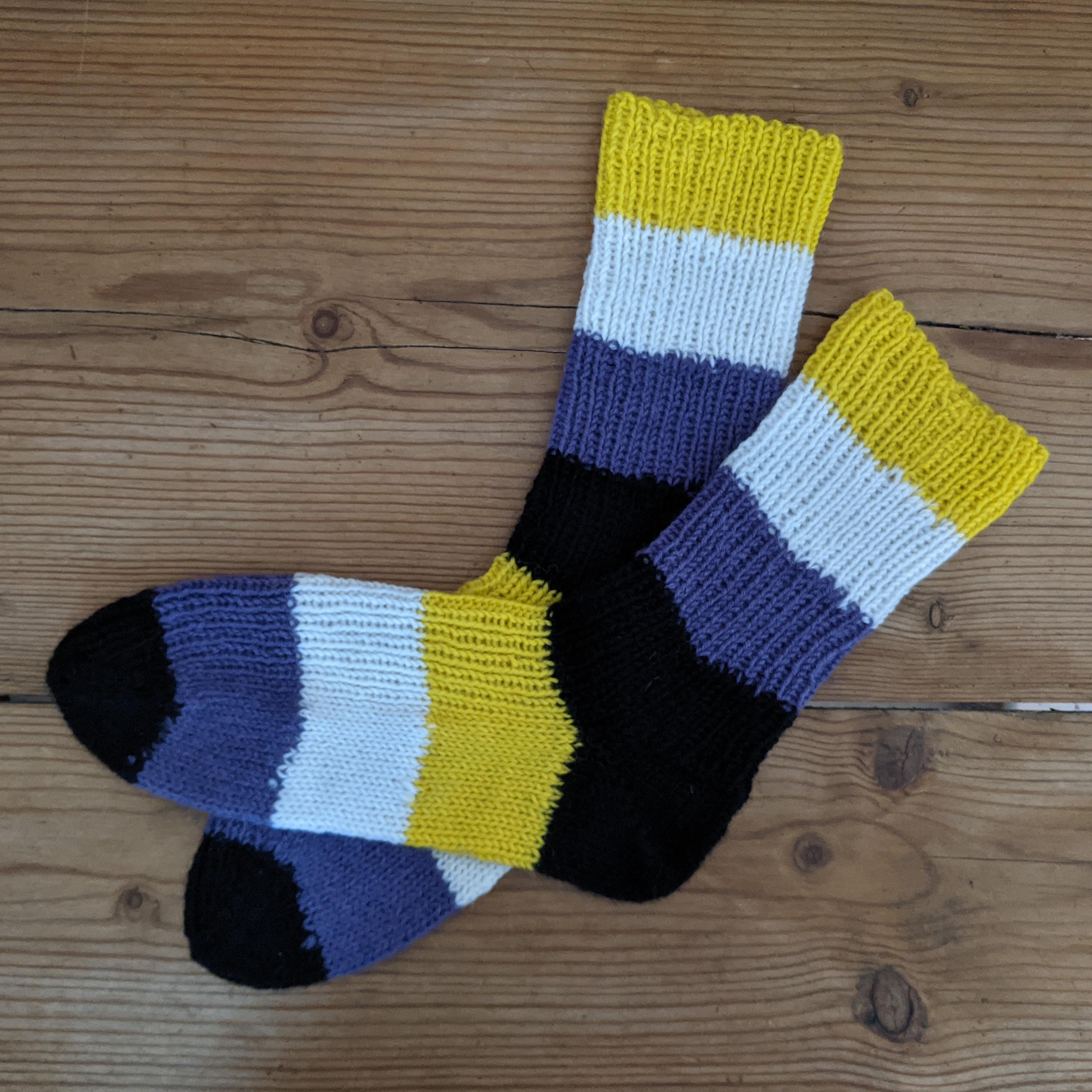 Pair of thick socks. Wide stripes from toe to cuff: Black, purple, white, yellow, heel, black, purple, white, yellow.