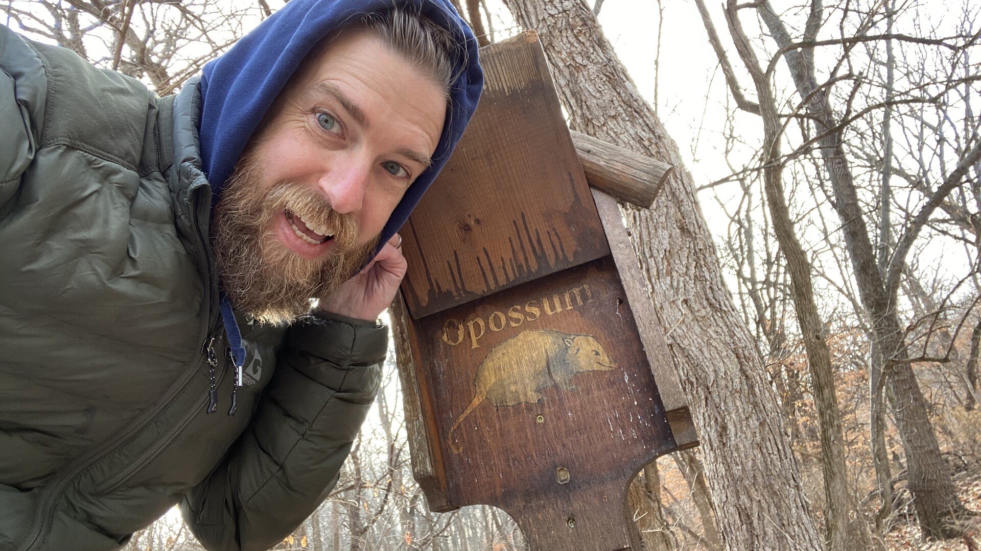 I am smiling in front of a wooden sign that says opossum 