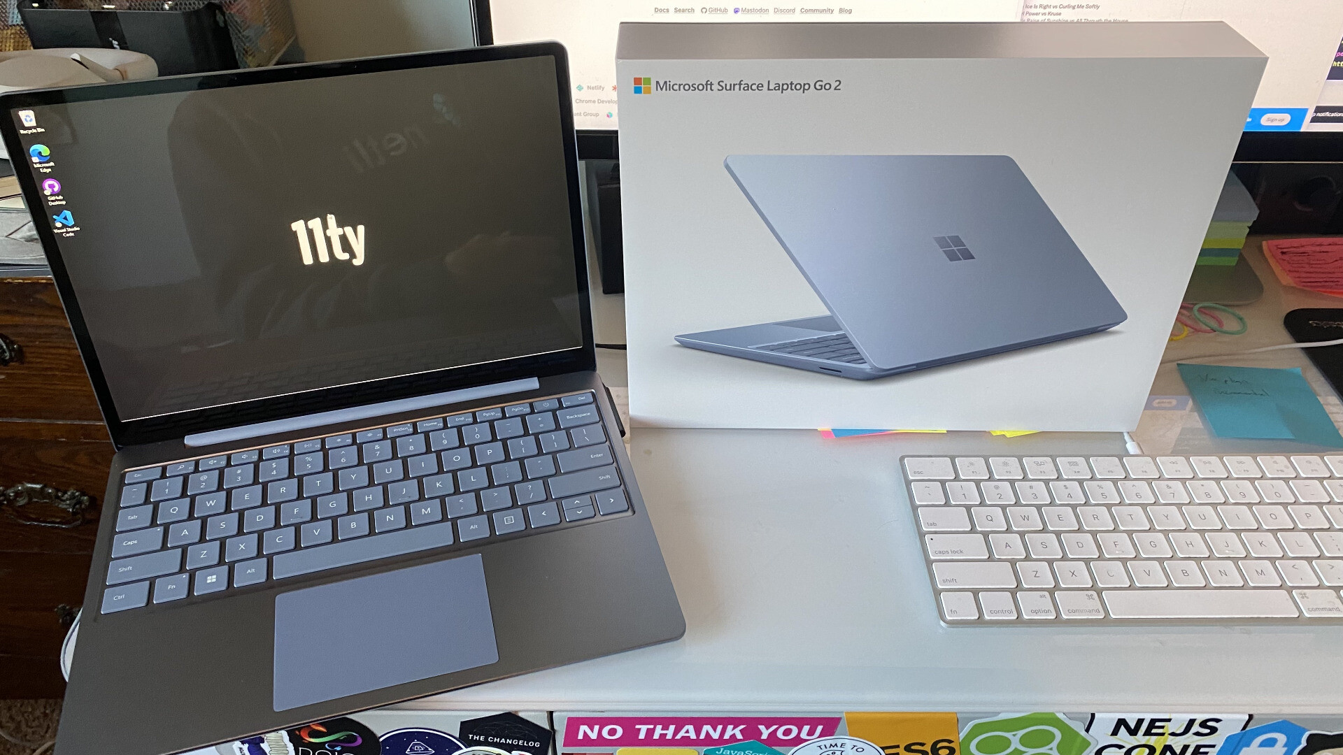 A photo of the Microsoft Surface Laptop Go 2 on my desk, opened up and showing the 11ty logo on the desktop. The box that it came in is set alongside