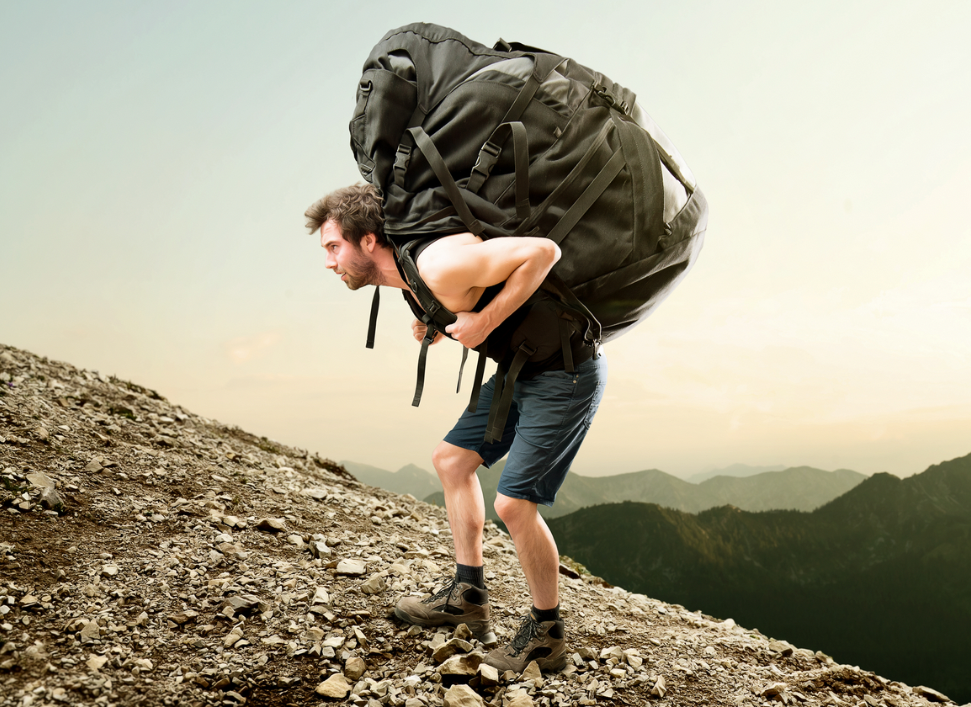 a man trying to walk up a rocky slope, hunched over with a comically large backpack