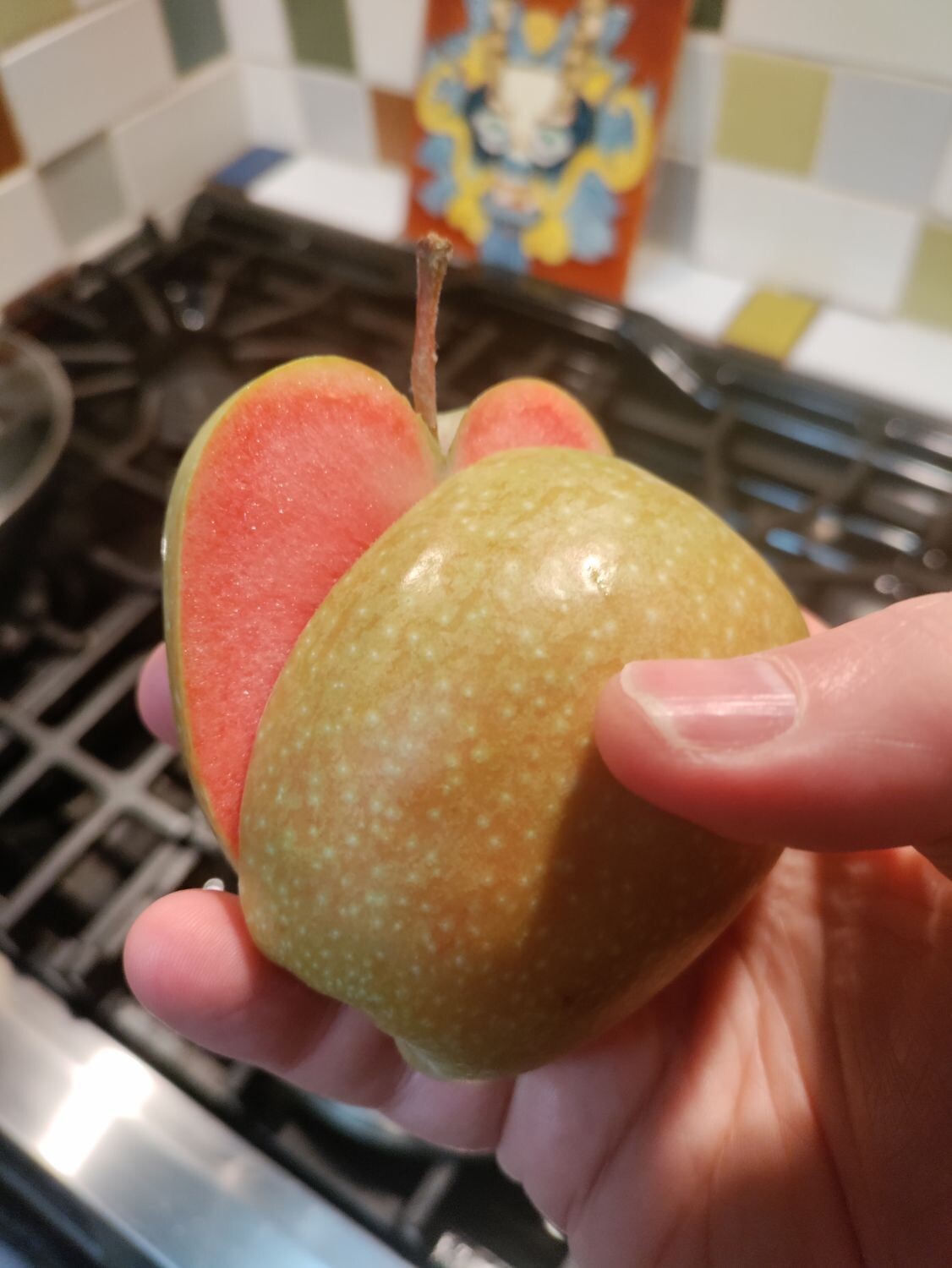 Two halves of an apple held in one hand. The skin of the apple is yellow but the flesh is pink.