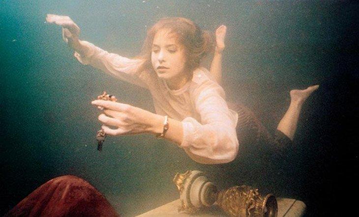 A woman swimming through a flooded room holding some jewelry just found