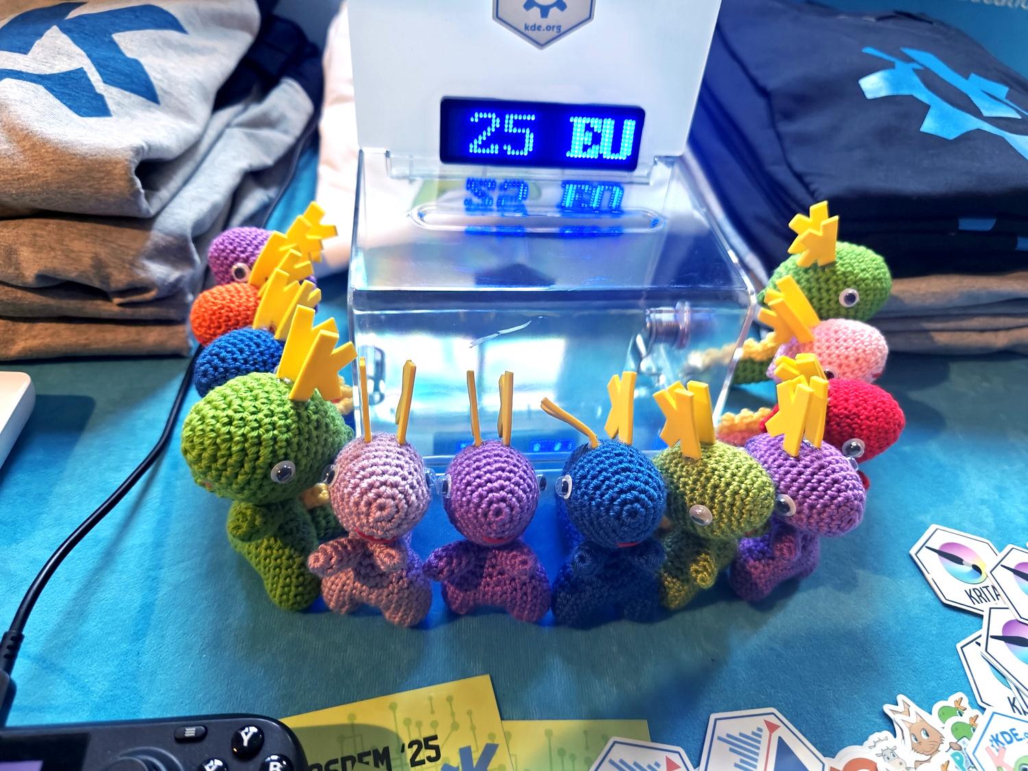 A bunch of crocheted multicoloured dragons are waiting to be adopted from KDE's FOSDEM booth.