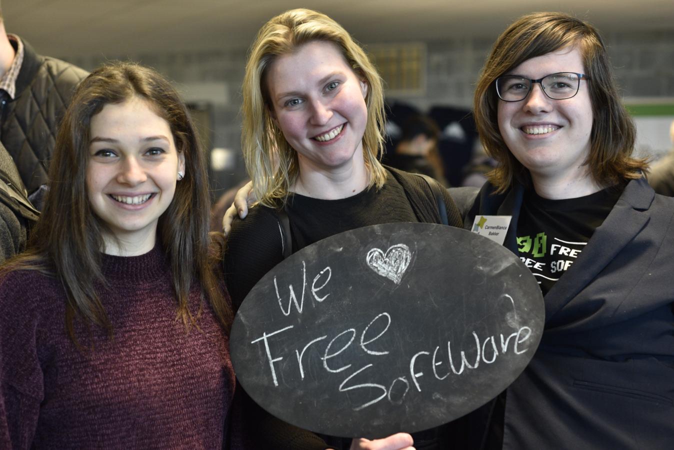Three smiley people hold up a sign that says "We ❤️ Free Software" at FOSDEM 2019.
Photo credit: Redazione Cultura. distributed under CC By SA license. Find the original and more at https://www.dgpixel.com/techblog/i-love-free-software-day-2019/