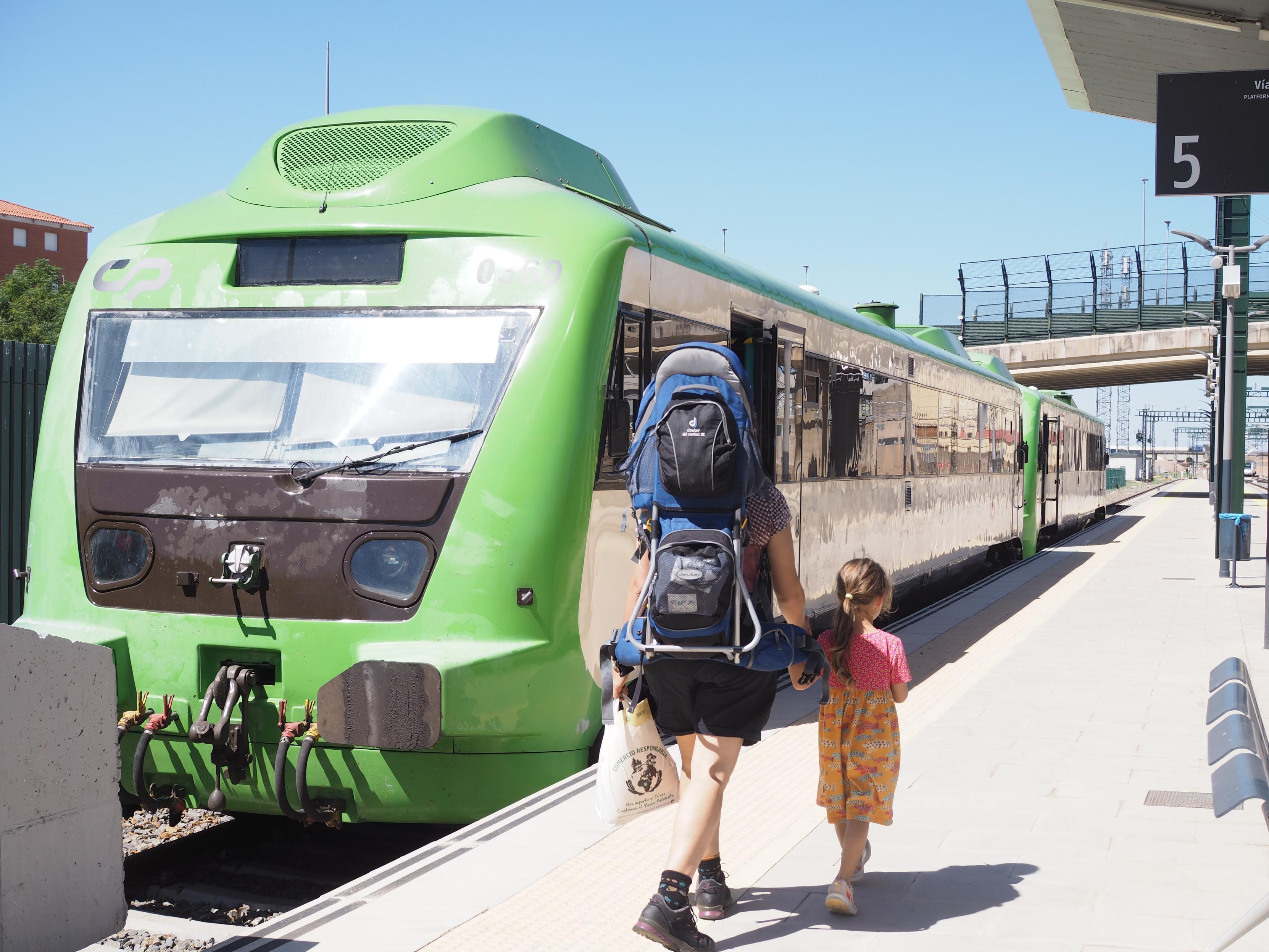 Green regional train at the station of Badajoz with my wife and daughter walking towards it along the platform with huge backpack on.