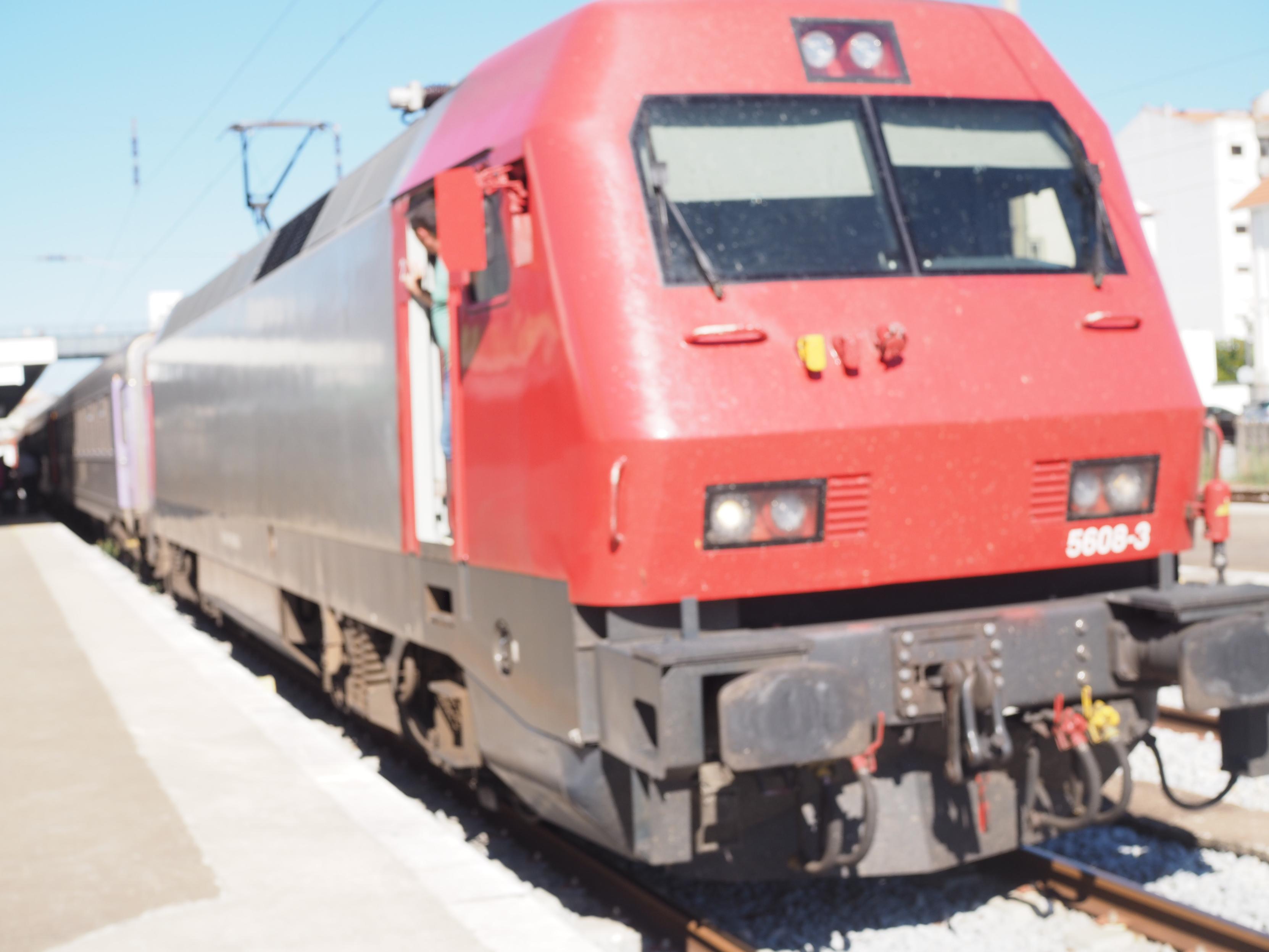 Diesel lokomotive with a red front waiting at a station with silver wagons behind it.