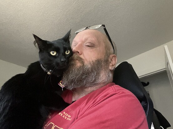 Molly, a black cat, holds her cheek against her humans face as he finally gives her the smooch she wanted.

