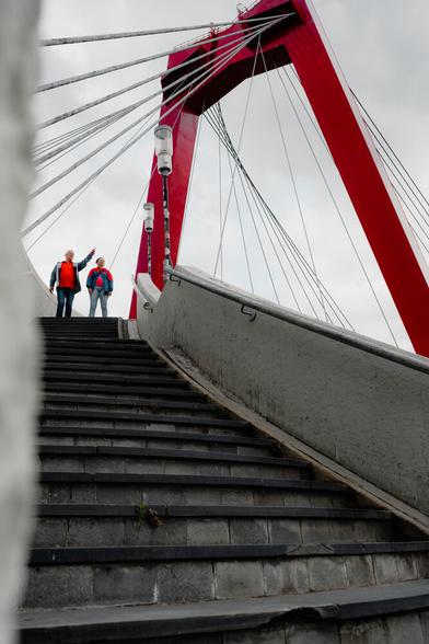 A staircase leading to a red bridge. Two people standing at the top of the stairs. One person is pointing into the distance.