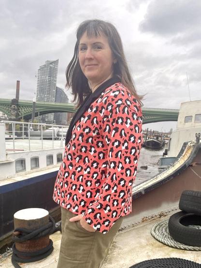 A white woman with straight brown hair is standing on the deck of a barge with her side to the camera. She's wearing a sweatshirt made from peachy-pink fabric with a repeating black and white print.