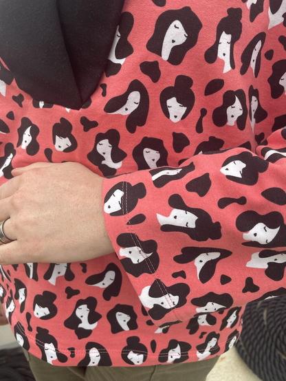 Detail of a sleeve of a sweatshirt made from peachy-pink fabric with a repeating black and white print.