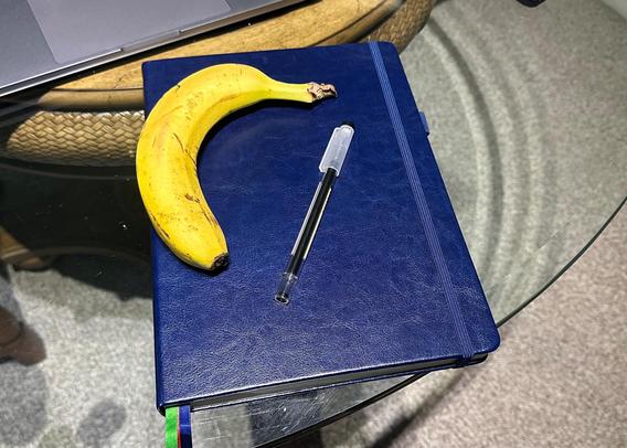Blue notebook with a pen and a banana on it for scale. The notebook is on a glass table top.