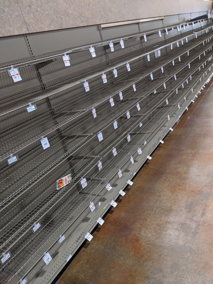 An entire supermarket isle of wire metal racks that are completely empty other than the white dangly price tags and a packet of taco seasoning randomly left on one shelf at a chaotic angle.