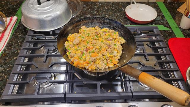 A wok with egg fried rice sitting in it, on top of a newly installed gas range with wok burner.