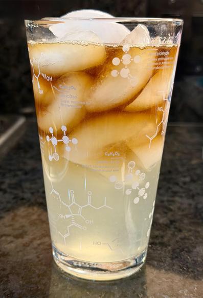 Glass is filled with a cloudy yellowish liquid at the bottom (pineapple ginger beer) and a dark liquid at the top - kraken rum. Lots of ice too. The glass is decorated with molecular diagrams of chemicals found in beer.