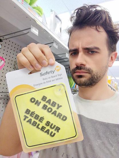 Man holding purchased yellow signs you would put in windshield: "baby on board" in english and "Bébé sur tableau" in french.