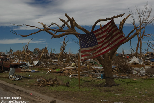 A US flag in a tree after the Greensburg tornado. All of the trees have been sandblasted and the ground is filled with rubble.