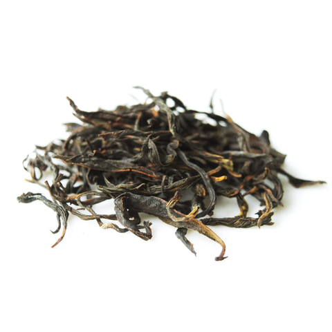 Close-up product-style photo of a small pile of loose dried tea leaves on a white background. The leaves are dark brown to black with some curled, twisted strands and a few lighter golden tips. Shallow depth of field keeps the center in focus while edges blur softly.