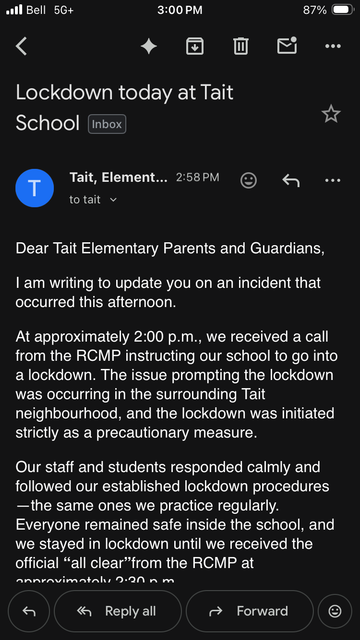 Screenshot of an email in dark mode on a phone screen. The subject line reads “Lockdown today at Tait School.” It is from Tait Elementary and marked Inbox, sent at 2:58 PM.

The visible message begins, “Dear Tait Elementary Parents and Guardians,” and explains that around 2:00 p.m. the school received a call from the RCMP instructing them to go into lockdown. It says the issue was occurring in the surrounding Tait neighbourhood and the lockdown was a precautionary measure.

The next paragraph states that staff and students responded calmly, followed established lockdown procedures, remained safe inside the school, and stayed in lockdown until receiving an official all-clear from the RCMP at approximately 2:30 p.m.

At the bottom are reply, reply all, and forward buttons. The phone status bar shows Bell 5G+, 3:00 PM, and 87% battery.