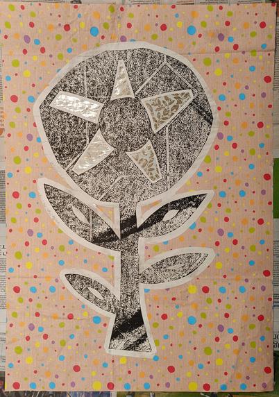 A large flower on spotty wrapping paper. The flower has a large head into which are set shiny leafy panels. The flower is printed with fading black ink, which shows the geometric pattern of the bathroom lino it was cut from. It's supposed to be a sunflower.