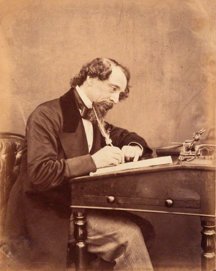 Dickens at his desk, 1858, by Herbert Watkins.

Dickens sits in profile at a writing desk, quill in hand, beard and curly hair characteristic of his middle years.

https://en.wikipedia.org/wiki/Charles_Dickens#/media/File:Dickens_by_Watkins_1858.png